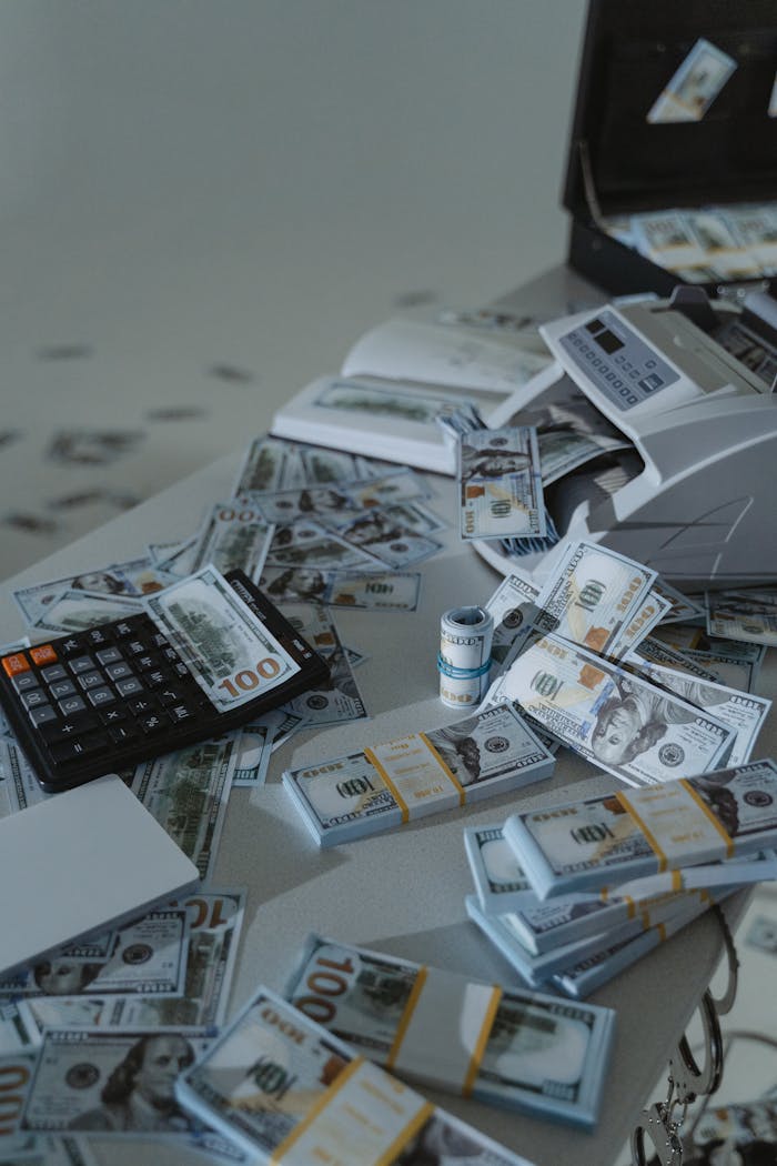 Image of US dollar bundles with a money counter and calculator on a white surface, conveying finance and business themes.